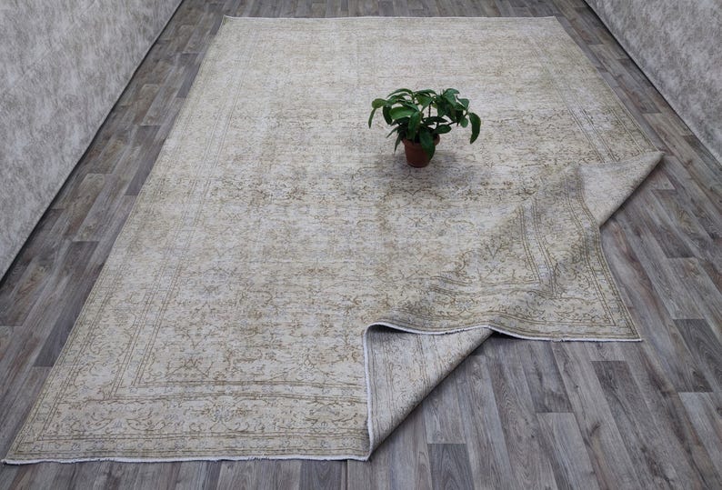 May include: A vintage-style rug with a faded floral pattern in shades of beige and green. The rug is folded in half and laid out on a wooden floor.