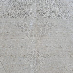 May include: A cream-colored rug with a delicate, intricate pattern in a darker shade of cream. The pattern features a central diamond shape with smaller diamond shapes surrounding it.