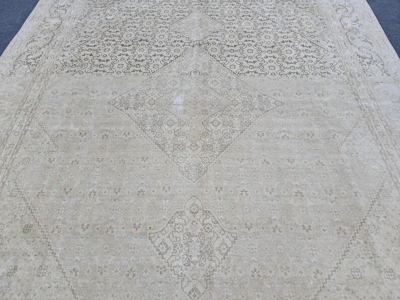 May include: A cream-colored rug with a delicate, intricate pattern in a darker shade of cream. The pattern features a central diamond shape with smaller diamond shapes surrounding it.