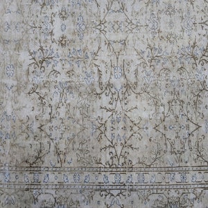 May include: A vintage rug with a faded floral pattern in shades of blue and brown on a white background. The rug has a border with a repeating geometric design.