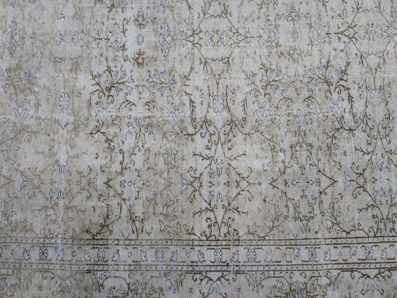 May include: A vintage rug with a faded floral pattern in shades of blue and brown on a white background. The rug has a border with a repeating geometric design.