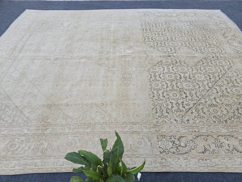 May include: A vintage cream-colored rug with a delicate floral pattern in black. The rug has a border with a more intricate design.
