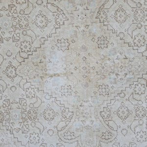 May include: A white rug with a delicate, intricate pattern in a light brown color. The pattern is made up of small, repeating motifs that create a subtle, elegant design.