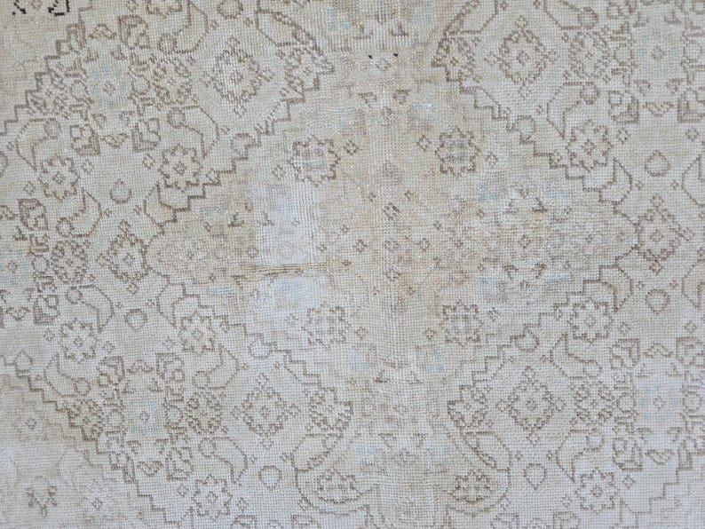 May include: A white rug with a delicate, intricate pattern in a light brown color. The pattern is made up of small, repeating motifs that create a subtle, elegant design.