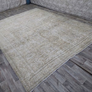 May include: A vintage cream-colored rug with a subtle floral pattern and a border. The rug is laid out on a wooden floor.