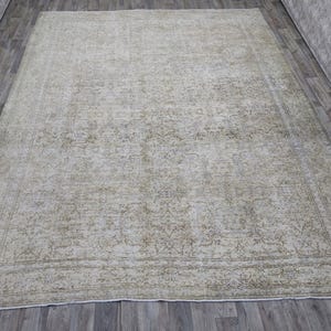 May include: A vintage rug with a faded floral pattern in shades of beige and green. The rug has a distressed look and a worn border.