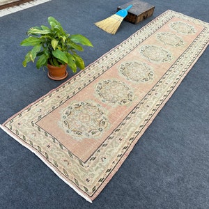 May include: A long, rectangular rug with a pink background and a repeating pattern of beige circles with intricate designs. The rug has a fringed edge.