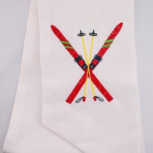 Puede incluir: Toalla de cocina blanca con esquís bordados en rojo y verde y bastones de esquí amarillos.