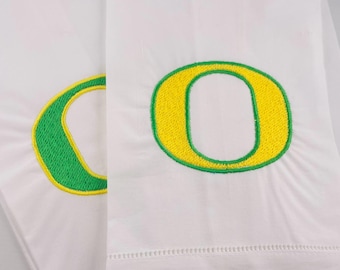 May include: Two white hand towels with green and yellow embroidered letter "O" designs.