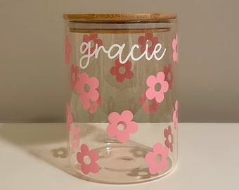 May include: A clear glass jar with a bamboo lid and pink flower decals. The jar is labeled "gracie" in white lettering.