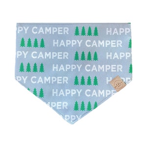 May include: A gray bandana with a white and green print of the words "Happy Camper" and pine trees. The bandana has a small brown label with the word "golden" on it.