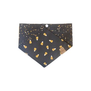 Puede incluir: Bandana negra con un bot&oacute;n blanco y un patr&oacute;n de ma&iacute;z dulce naranja y blanco sobre un fondo negro. La bandana tiene una etiqueta marr&oacute;n con el texto "Pawsitive Vibes" en ella.
