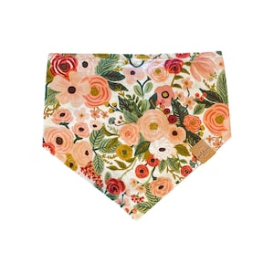 Puede incluir: Un pañuelo blanco con estampado floral con flores rosas, rojas y verdes. El pañuelo tiene una etiqueta de cuero marrón con el texto "Golden" en ella.