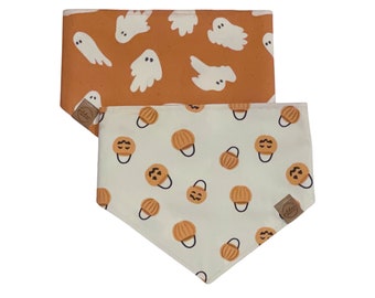 May include: Two Halloween-themed dog bandanas. One is orange with white ghost illustrations. The other is cream-colored with orange pumpkin illustrations. Both bandanas have a brown tag with a logo.