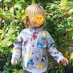 May include: A child wearing a gray fleece jacket with a colorful animal print. The jacket has a button closure and a stand-up collar.