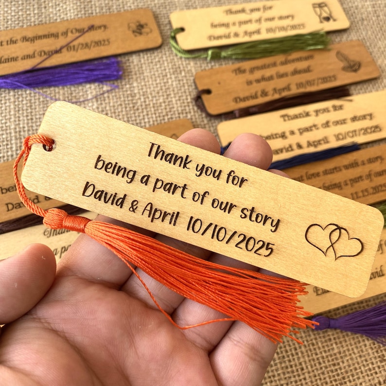 May include: Wooden bookmark with a tassel, engraved with the text "Thank you for being a part of our story David & April 10/10/2025" and two intertwined hearts.