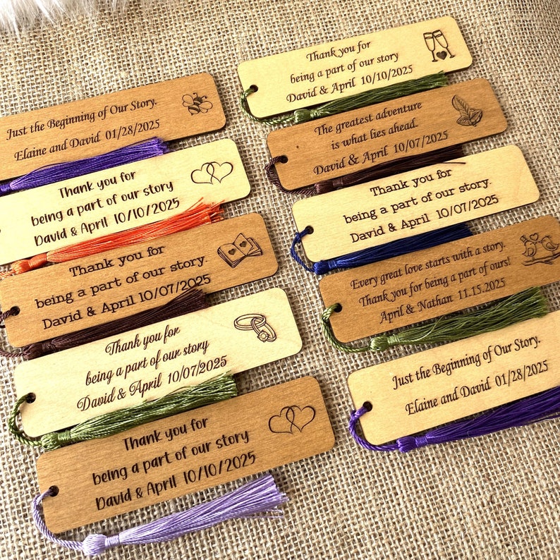 May include: A set of 10 wooden bookmarks with different designs and text. Each bookmark has a tassel attached to the bottom. The text on the bookmarks includes "Thank you for being a part of our story" and the names "David & April" along with a date. Some bookmarks also include a design such as a heart, a book, or a bird.