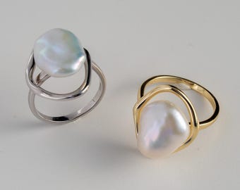 May include: Two rings with large, irregular-shaped pearls. One ring is silver-toned, and the other is gold-toned. The pearls have a lustrous, iridescent sheen. The rings have a modern, minimalist design, with the pearl as the focal point.