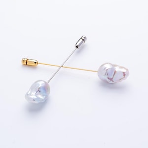 Peut inclure: Deux épingles de revers en perles avec des finitions argentées et dorées. Les épingles présentent des perles irrégulières et iridescentes. Une épingle a une base dorée, tandis que l'autre a une base argentée. Les épingles sont posées sur un fond blanc.