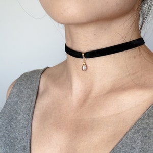 May include: A black velvet choker necklace with a small, light pink pearl pendant.