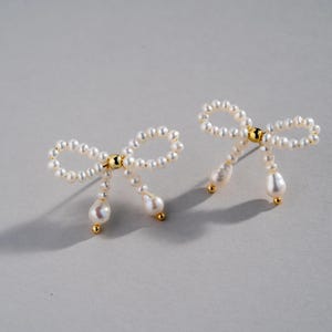 May include: A pair of pearl earrings shaped like bows with dangling pearl drops.