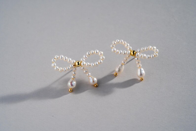 May include: A pair of pearl earrings shaped like bows with dangling pearl drops.