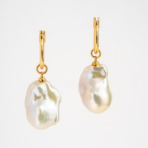 May include: A pair of gold hoop earrings, each suspending a large, irregularly shaped white pearl. The pearls have a lustrous, iridescent sheen, reflecting hints of pink and green. The earrings are set against a plain white background.