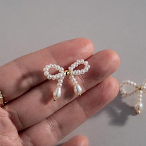 May include: A pair of pearl bow earrings with gold accents. The earrings are small and delicate, and they would make a great gift for a special occasion.