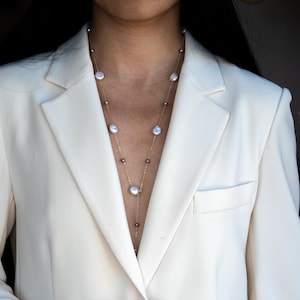 Puede incluir: Un collar largo de cadena dorada con perlas blancas y rosadas. El collar está formado por dos hileras de perlas, una con perlas más grandes y otra con perlas más pequeñas.