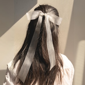 Könnte beinhalten: Ein weißes, durchsichtiges Band, das zu einer Schleife gebunden ist und als Haarschmuck verwendet wird.