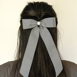 May include: A black and white checkered bow with a pearl-like embellishment in the center, tied in a person's long black hair.