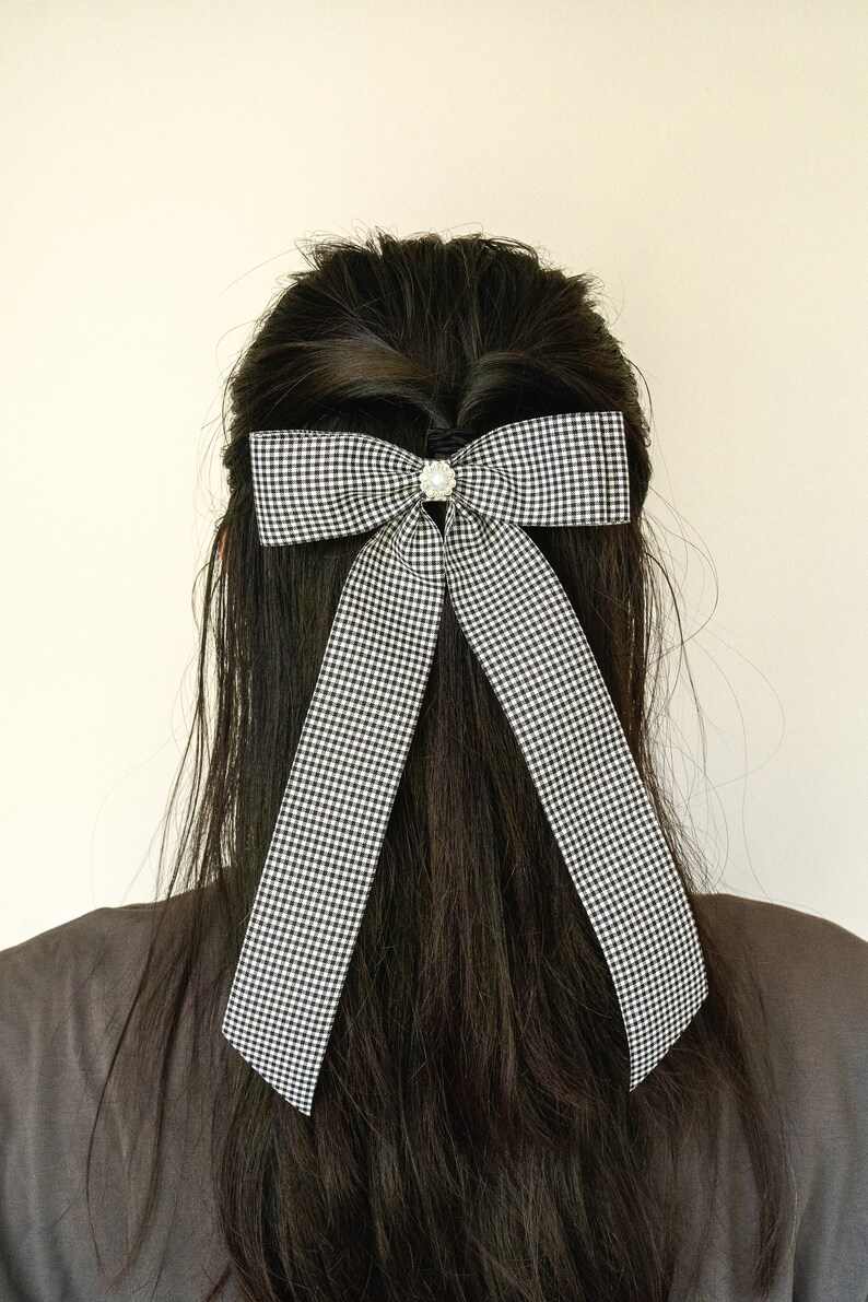 May include: A black and white checkered bow with a pearl-like embellishment in the center, tied in a person's long black hair.