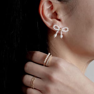 May include: A pair of pearl earrings in the shape of a bow, and a gold ring with a row of pearls and a row of cubic zirconia stones.