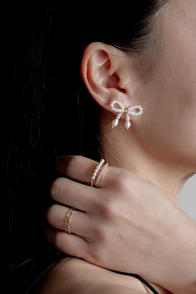 May include: A pair of pearl earrings in the shape of a bow, and a gold ring with a row of pearls and a row of cubic zirconia stones.