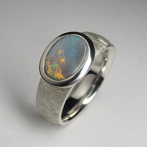 May include: A silver ring with a textured band and an oval-shaped opal gemstone set in a bezel setting.