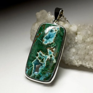 Può includere: Un ciondolo d'argento con una pietra di crisocolla verde e blu con un motivo unico. La pietra è incastonata in una cornice d'argento e pende da una catena d'argento.