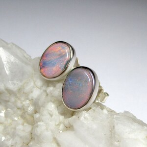 May include: A pair of silver opal earrings with a light pink and white opal stone. The earrings are set on a white background.