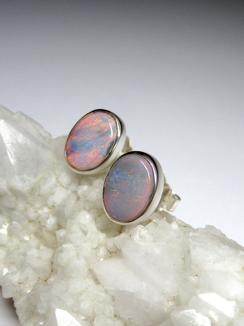 May include: A pair of silver opal earrings with a light pink and white opal stone. The earrings are set on a white background.