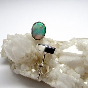 May include: A pair of silver stud earrings with oval-shaped green opal gemstones. The earrings are set on a white background.