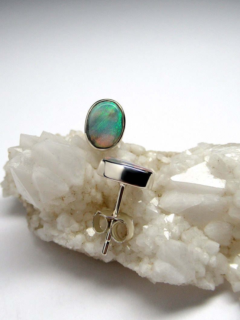 May include: A pair of silver stud earrings with oval-shaped green opal gemstones. The earrings are set on a white background.