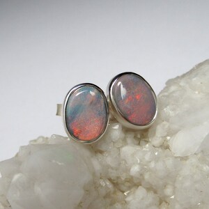 May include: A pair of silver opal earrings with oval-shaped stones. The opals have a white base with flashes of red and orange.