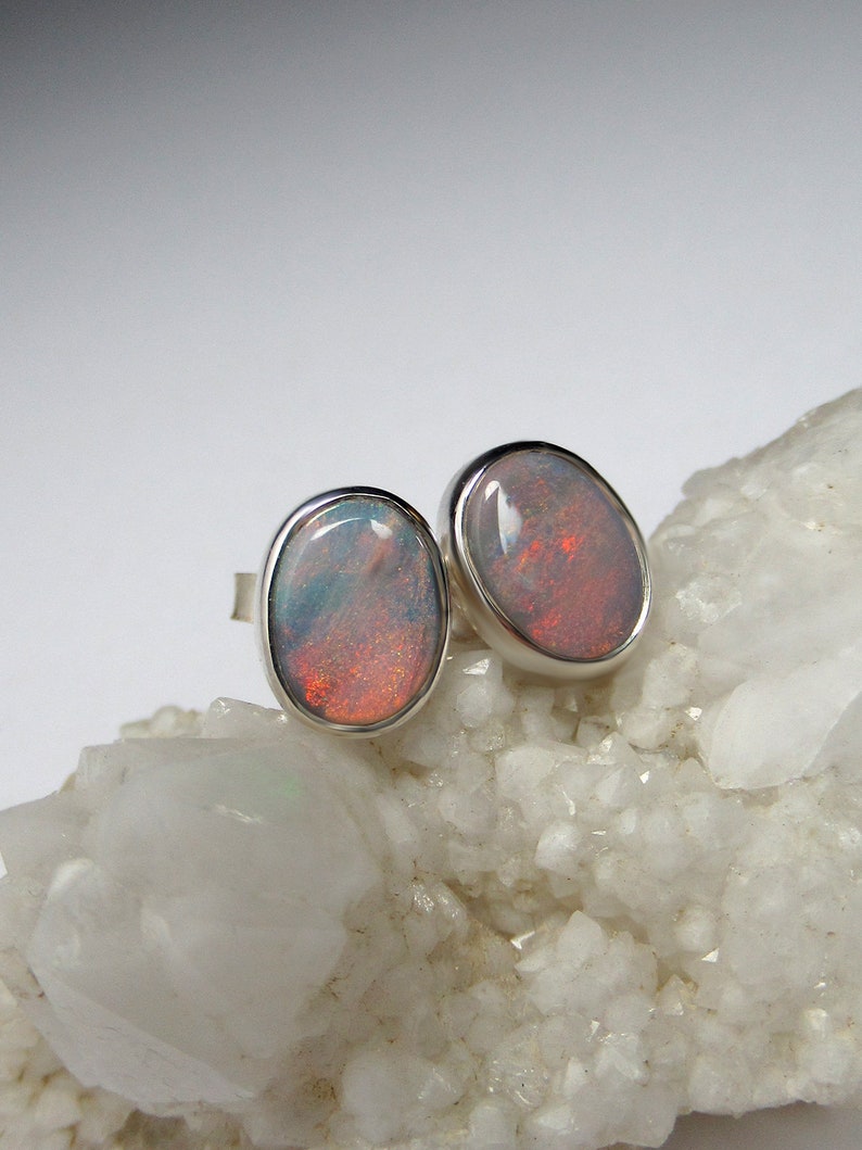 May include: A pair of silver opal earrings with oval-shaped stones. The opals have a white base with flashes of red and orange.