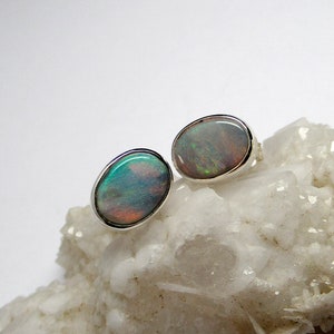 May include: A pair of silver opal earrings with a white background. The opals are oval shaped and have a iridescent sheen.