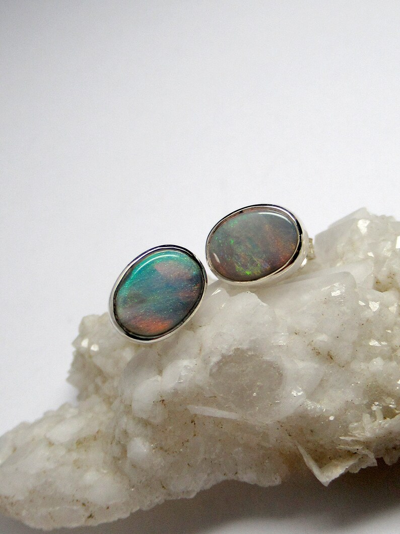 May include: A pair of silver opal earrings with a white background. The opals are oval shaped and have a iridescent sheen.