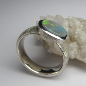 May include: A silver ring with a textured band and a light green opal gemstone set in a bezel setting.