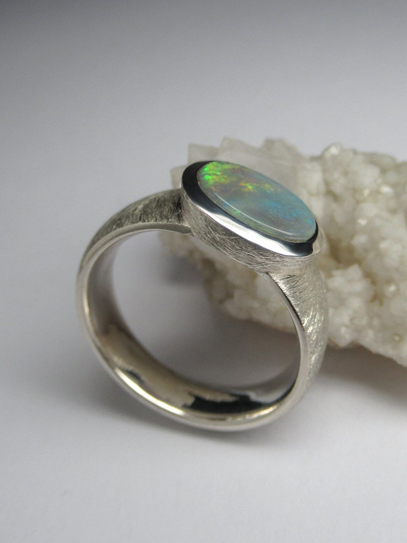 May include: A silver ring with a textured band and a light green opal gemstone set in a bezel setting.