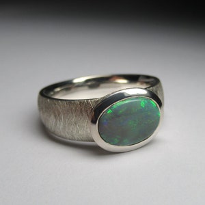 May include: A silver ring with a textured band and a green opal gemstone.