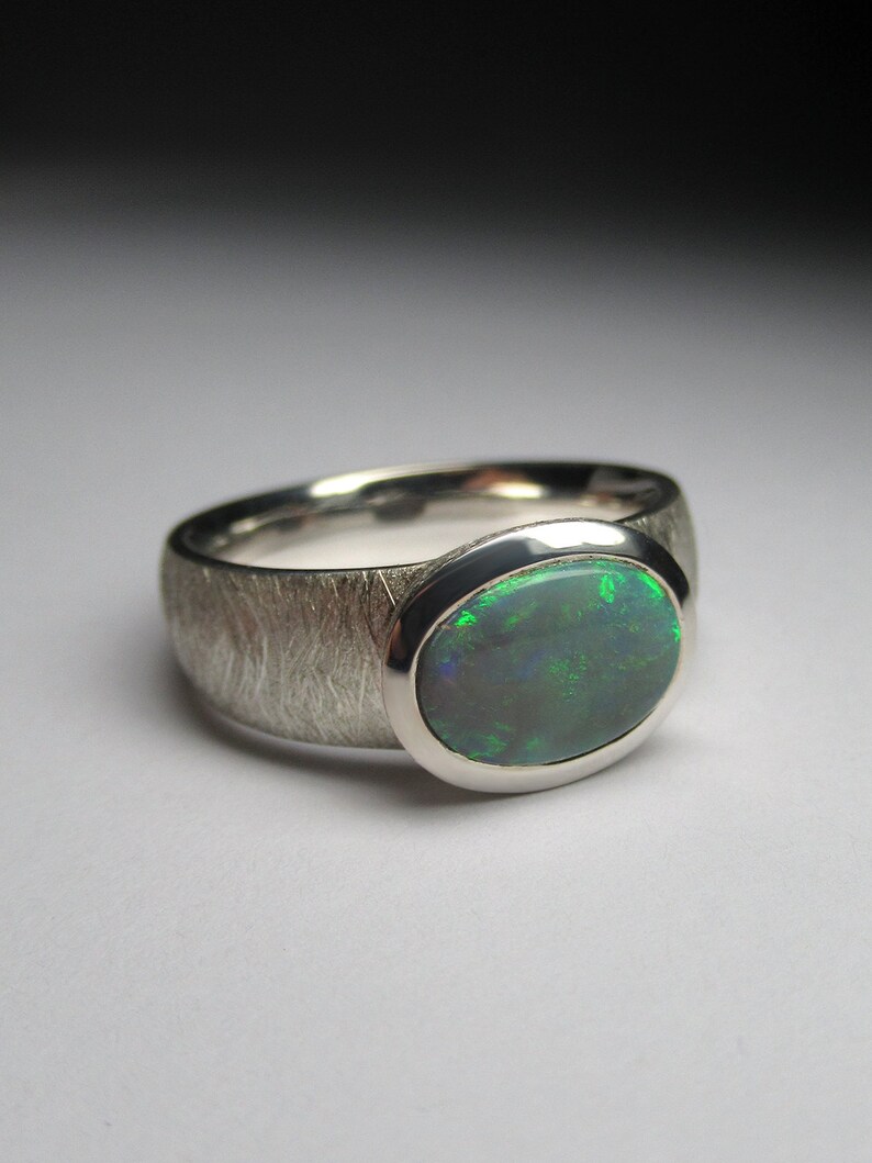 May include: A silver ring with a textured band and a green opal gemstone.