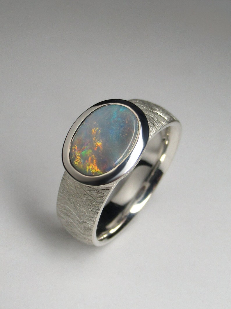 May include: A silver ring with a textured band and an oval-shaped opal gemstone set in a bezel setting.