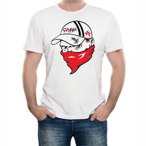 May include: White t-shirt featuring a graphic of a person wearing a baseball cap and a red bandana. The cap has the word "SARSI" and an eagle design. The person's face has a stern expression.